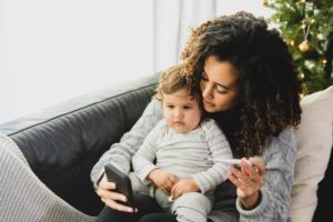 Mother sitting with baby on her lap with thermometer in hand 