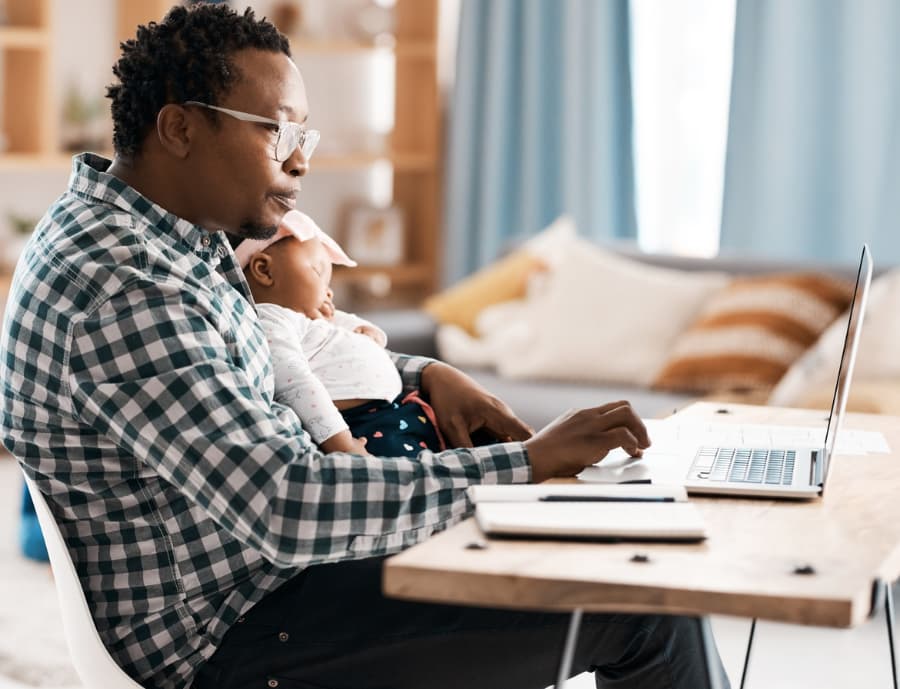 Parent holding sleeping child while researching on laptop